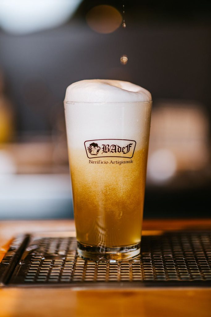 Bicchiere logato Badef pieno di birra chiara sulla griglia del bancone