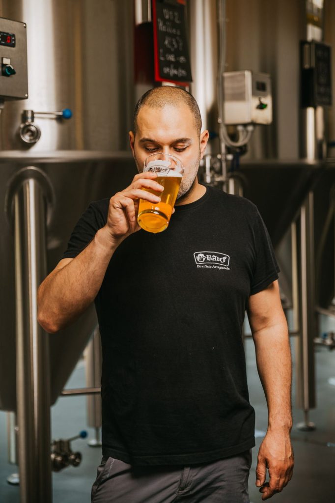 Birraio che assaggia una birra fra i serbatoi del birrificio Badef