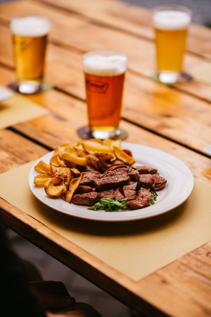 Piatto di tagliata con patatine e due birre sul tavolo del Brew Pub Badef