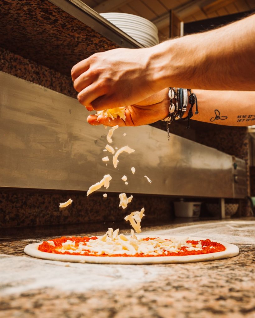 Il pizzaiolo condisce la pizza sulla pala
