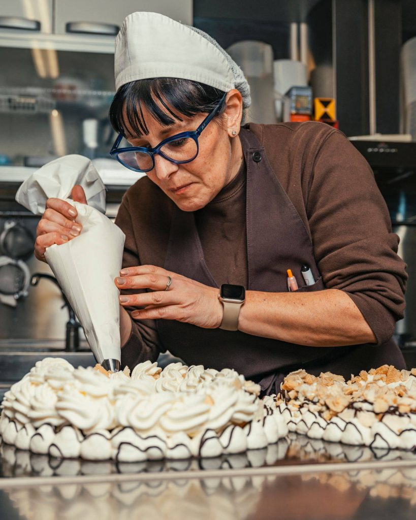 Pasticcera che decora con la sac à poche il bordo di una torta meringata