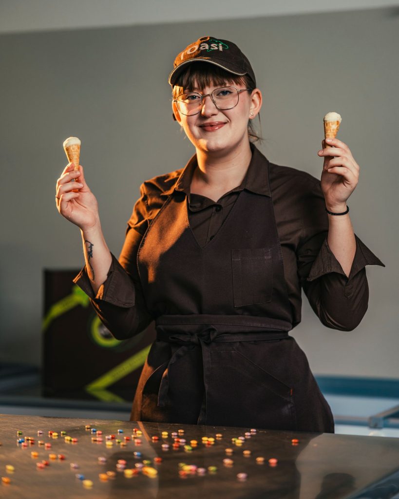 Ragazza dello staff dietro al banco con due coni di gelato in mano
