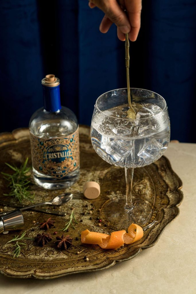 Mani che preparano un drink con Gin Cristallo, con cucchiaio da bar e ghiaccio