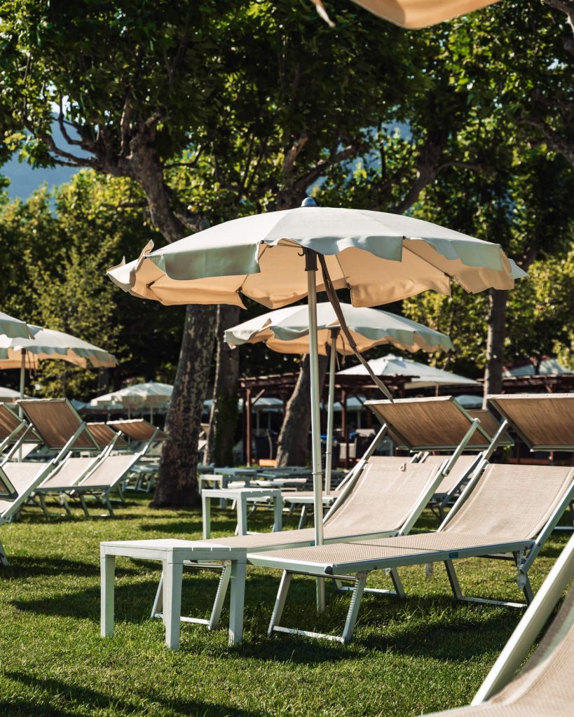 Prato del Lido Iseo con lettini e ombrelloni all'ombra degli alberi