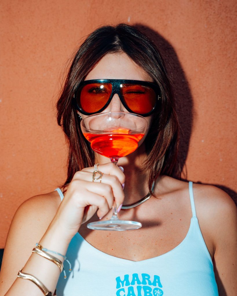 Ragazza con canotta Maracaibo beve un cocktail alla serata