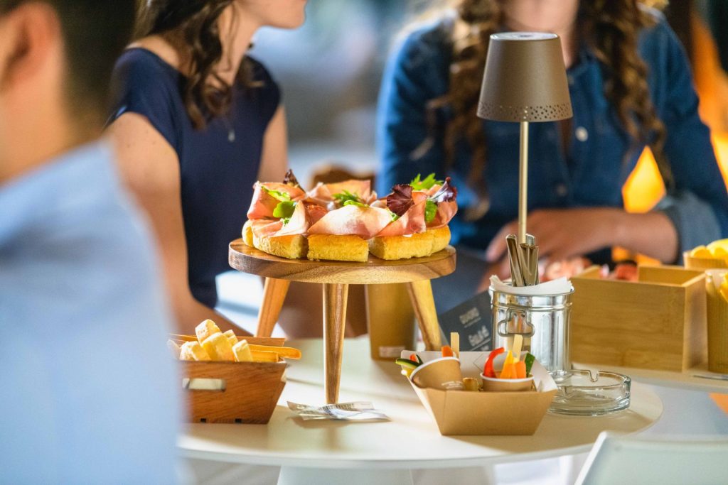 Due clienti all'aperitivo con l'alzata di taglieri e stuzzichini