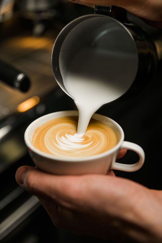 Il barista versa il latte e disegna la foglia sul cappuccino