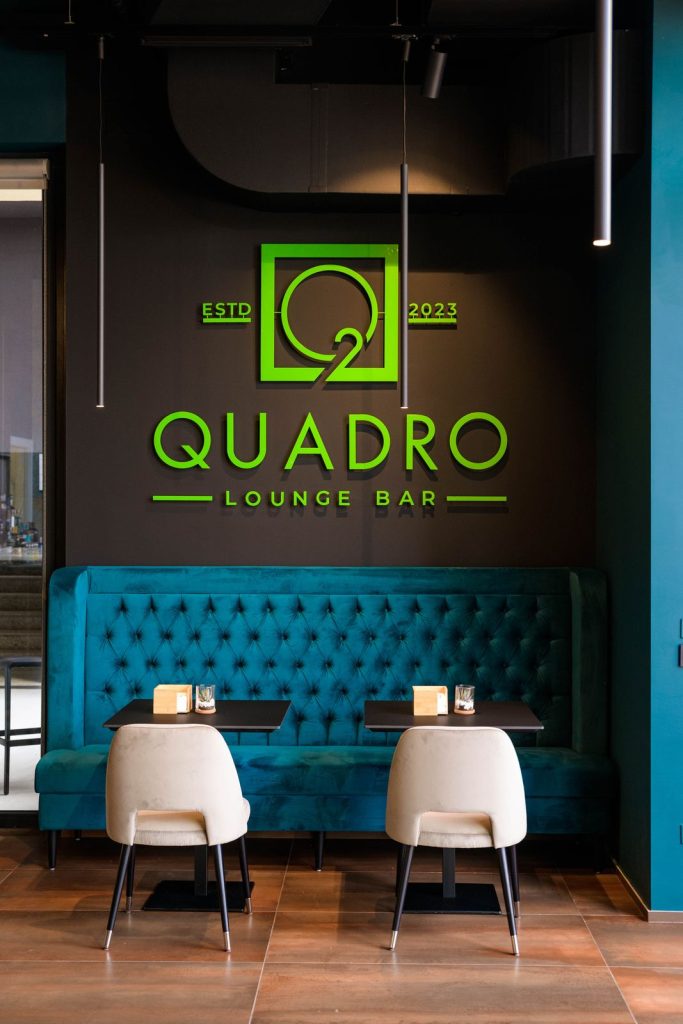 L’insegna verde Quadro Lounge Bar sopra il divano in velluto