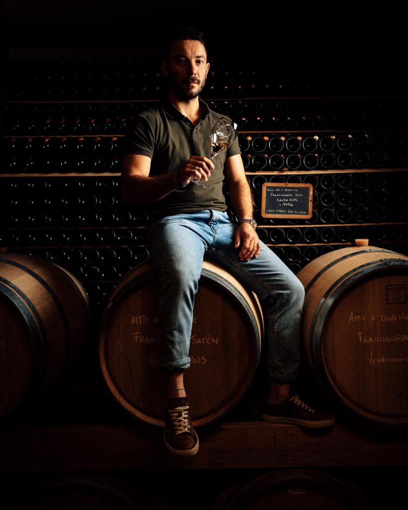 Ritratto sulle botti della cantina, con un calice di Franciacorta in mano