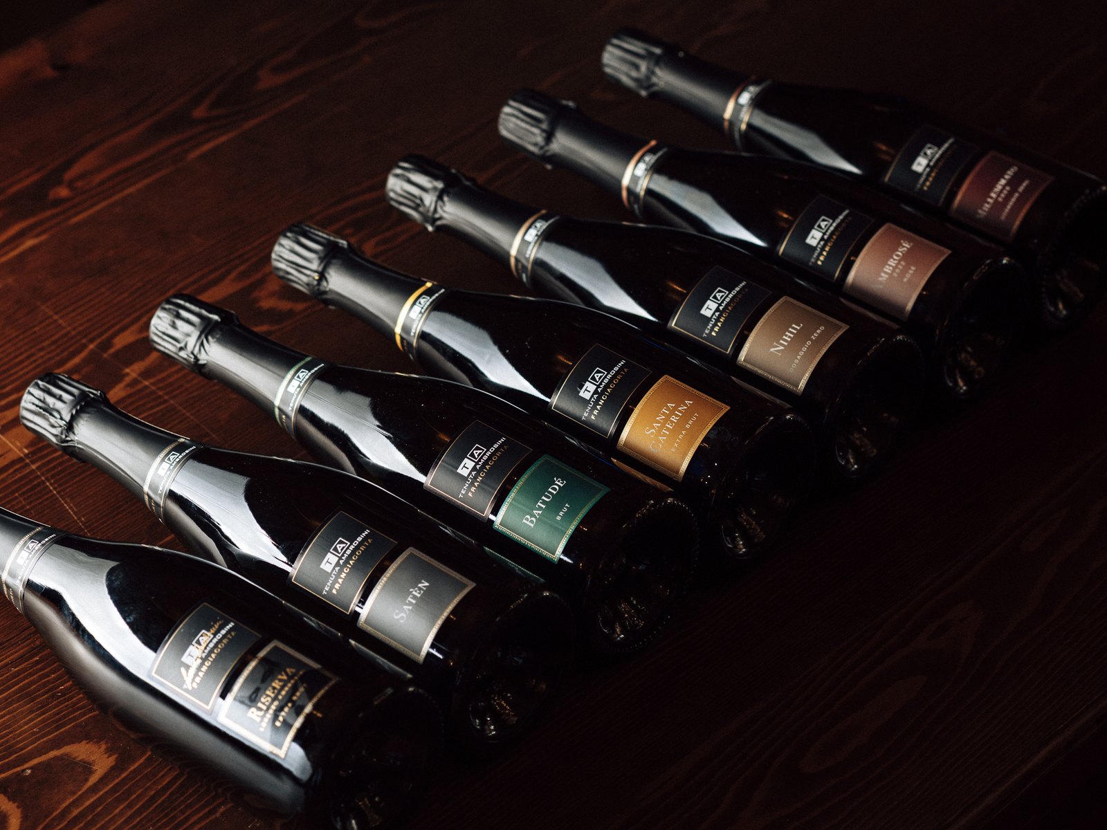 Le bottiglie di Franciacorta di Tenuta Ambrosini fotografate su un tavolo in legno