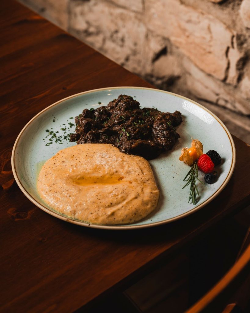 Brasato con polenta servito su un tavolo in legno davanti al muro in pietra del Ristorante La Torre